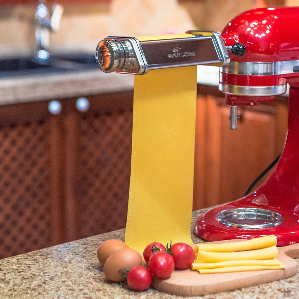 Gvode pasta roller attachment on red stand mixer with fresh pasta sheet, eggs, and tomatoes