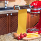 Gvode pasta roller attachment on red stand mixer with fresh pasta sheet, eggs, and tomatoes